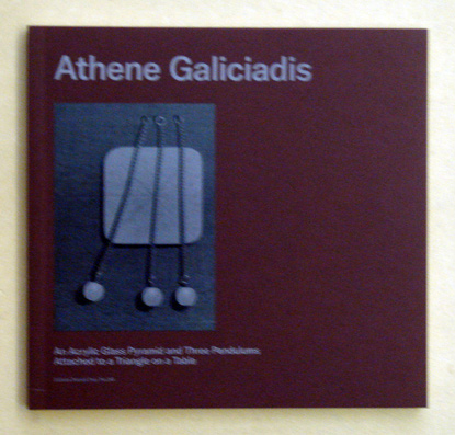 Athene Galiciadis - An Acrylic Glass Pyramid and Three Pendulums attached to a Triangle on a Table